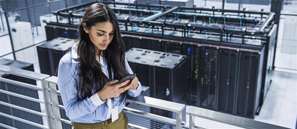Woman looking at her mobile phone in a room full of servers.